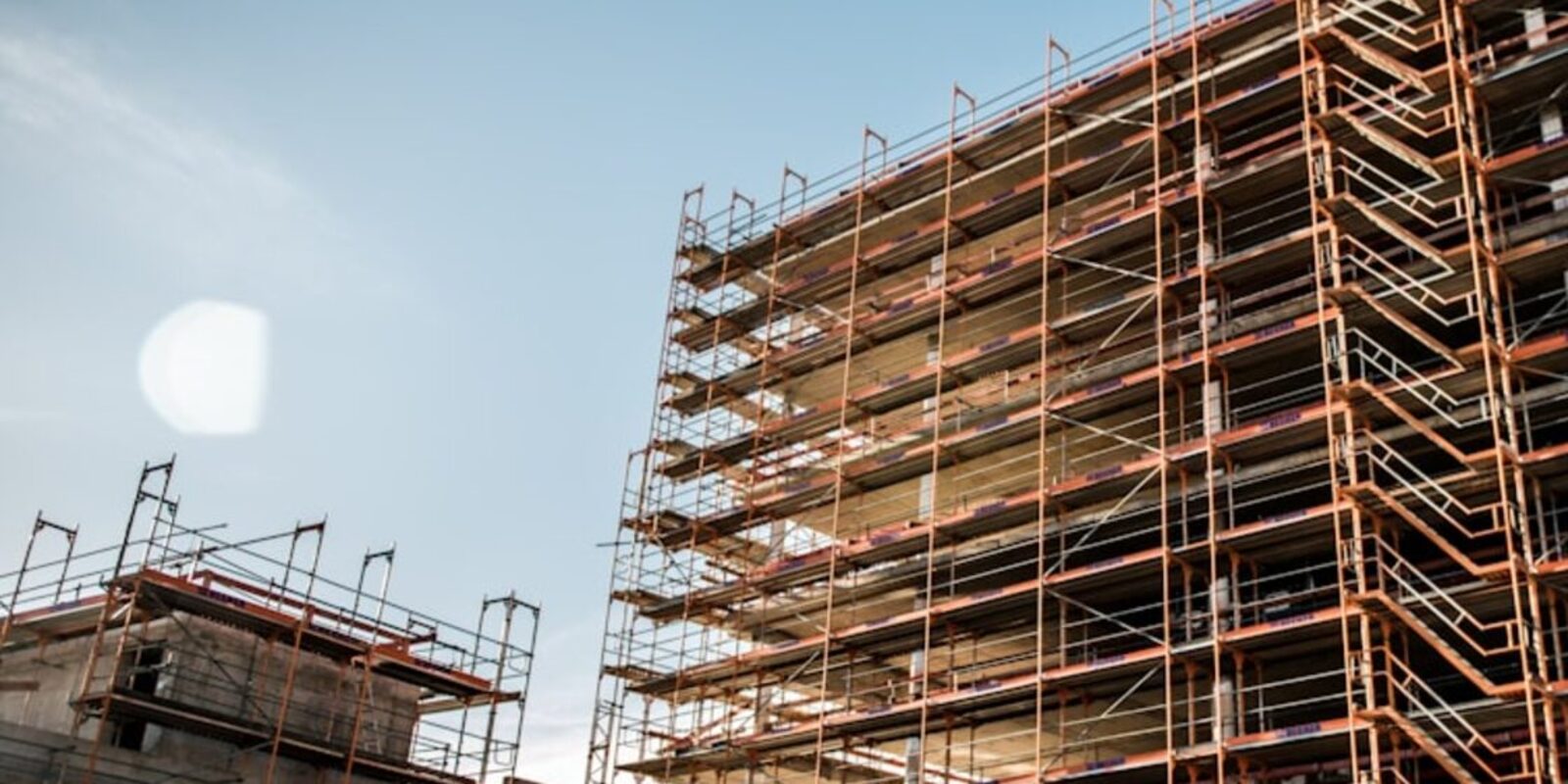 Multi-storey building elevation wrapped in tube-and-board scaffolding against a clear sky